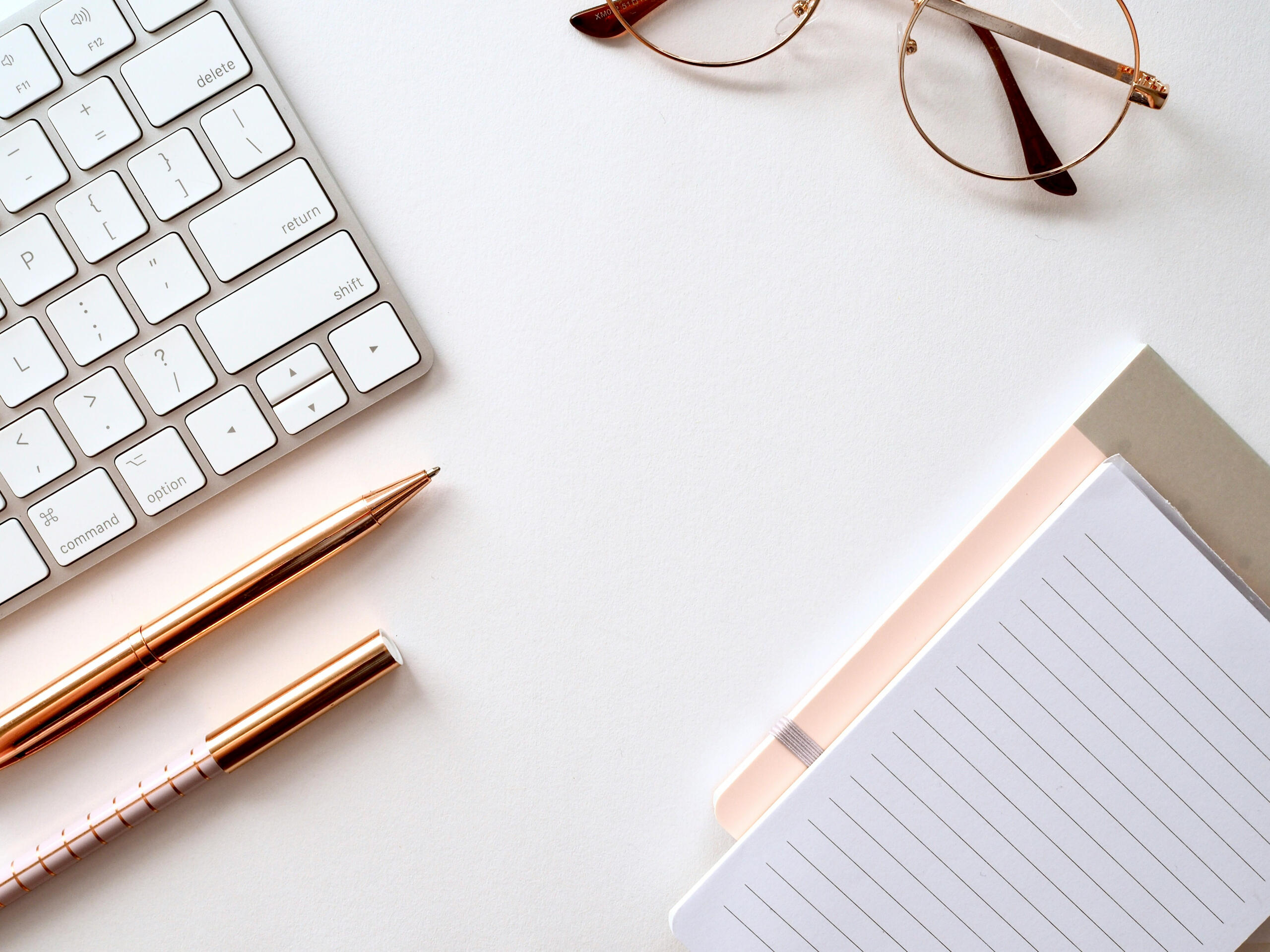A picture of a desk top with keyboard, two notebooks and two fancy pens.
